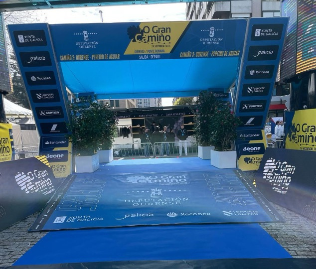 Arco de partida do O Gran Camiño com tapete azul e sinalética